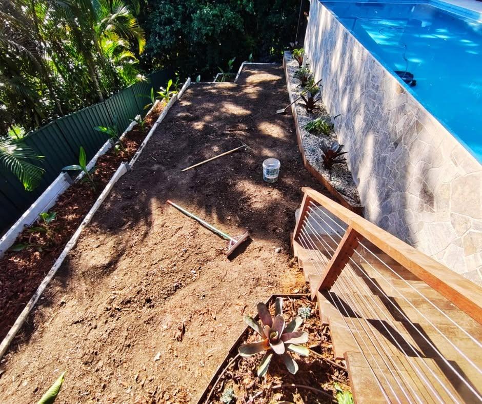 Terraced garden beds being prepared beside a pool and timber stairs