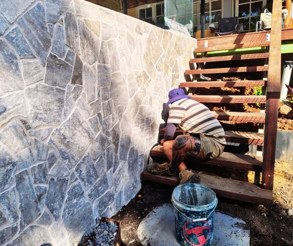 AJ team member working beside a natural stone wall and timber stairs
